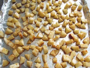 Raw potatoes coated in oil, seasoned and spread out evenly on a baking sheet