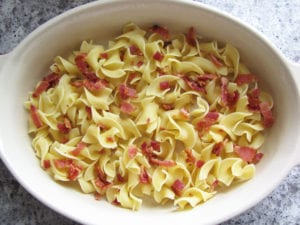 Cooked noodles in baking dish with bacon